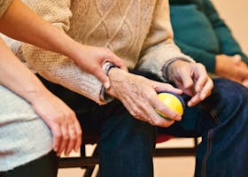 An elderly person receives support from a caregiver, holding hands indoors, showcasing compassion.