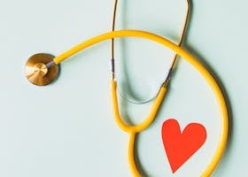 Yellow stethoscope arranged with a red heart cutout on a light green background, symbolizing heart health.